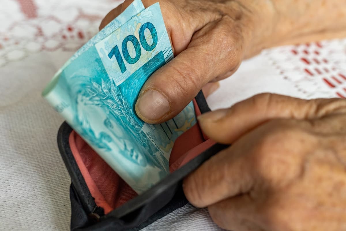 mãos em destaques de um idoso guardando dinheiro na carteira pagamento do inss